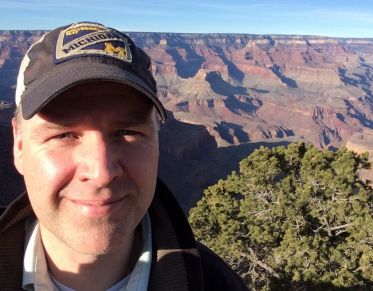 Man in ball cap smiles at the camera in front of the Grand Canyon.