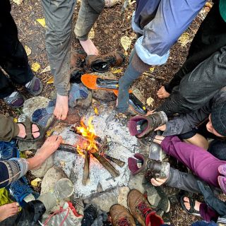 Students warm their feet and dry their boots around a campfire