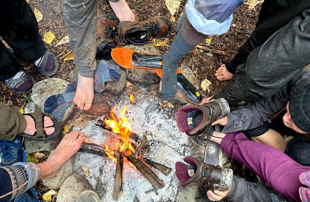 Students warm their feet and dry their boots around a campfire