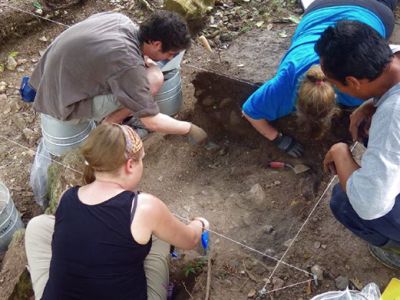 People bending over around hole dug in ground.