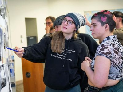 Two people engaged in discussion while analyzing black and white photographs on a display board. One person points at a photo, while the other listens attentively