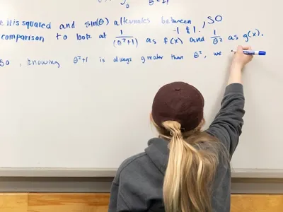 a student works a math equation at a whiteboard using a blue marker