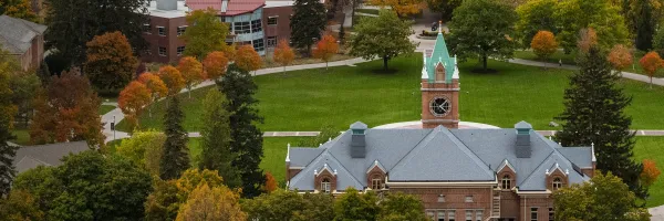 A picture of Main Hall with a pumpkin and trees with changing fall colors.