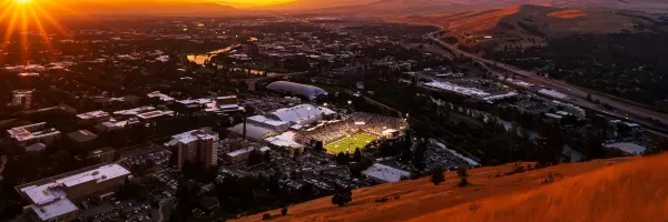 The sun sets over Missoula with Washington-Grizzly Stadium glowing under the lights down below.