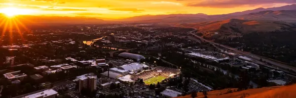 The sun sets over Missoula with Washington-Grizzly Stadium glowing under the lights down below.