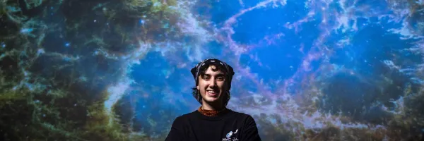 A UM student poses in front of a celestial image projected in �Թ���'s Planetarium.