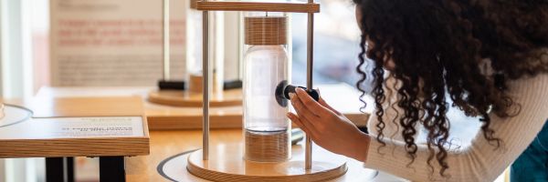 person playing with a magnet and iron filings inside a glass cylindar 