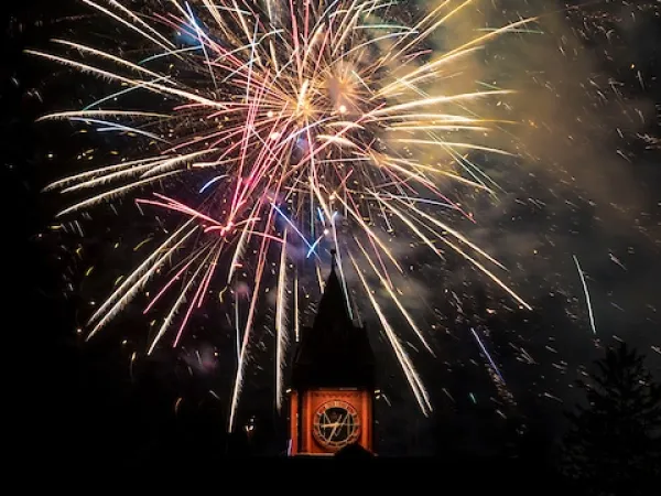 The University of Montana's Main Hall clock tower is lit up at night from Fireworks exploding above.