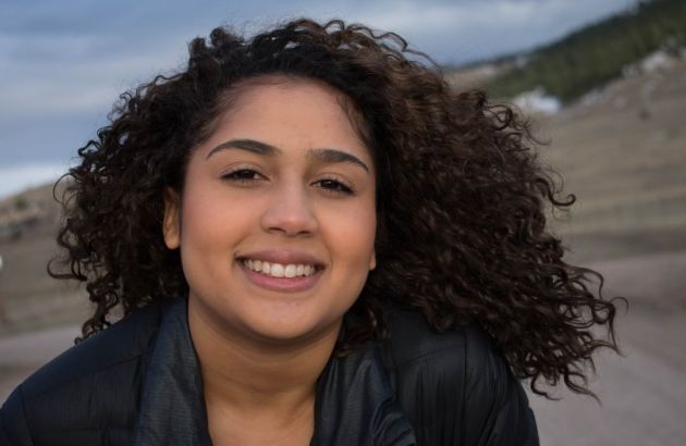 Woman with curly brown hair at the top of mountain. 