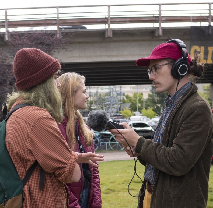 Man with microphone interviews woman in stocking cap outside.