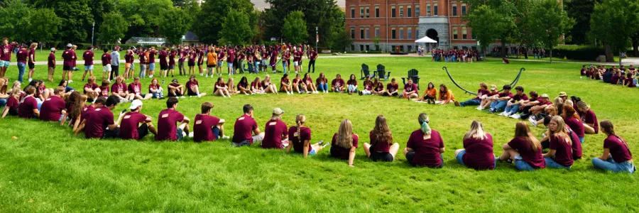 large group of students in maroon t-shirts sitting in a circle on the UM oval