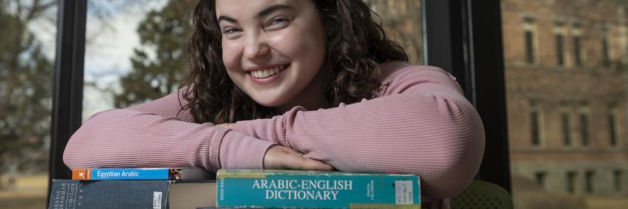 student smiling with arms crossed over several Arabic language textbooks