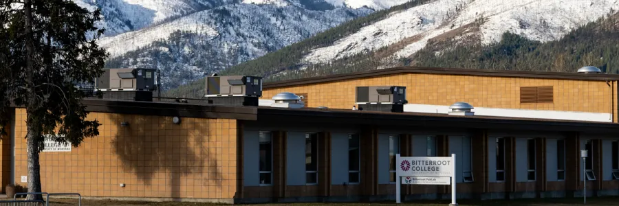 outside view of Bitterroot College building and sign with snow covered mountains in the background