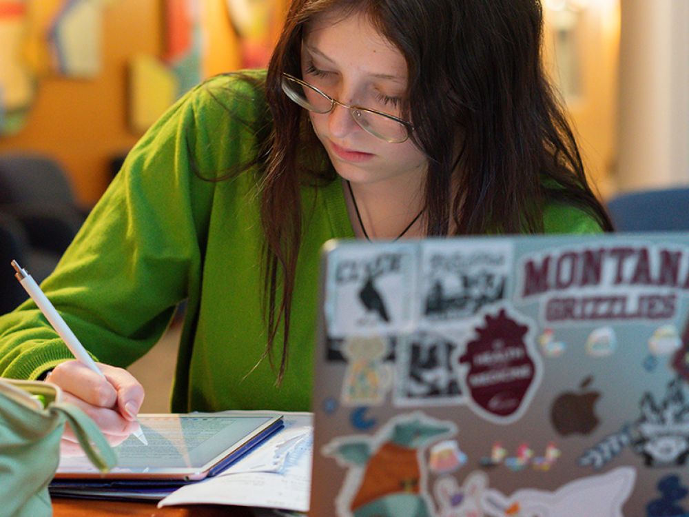 A student takes notes on a digital tablet with a laptop in the foreground