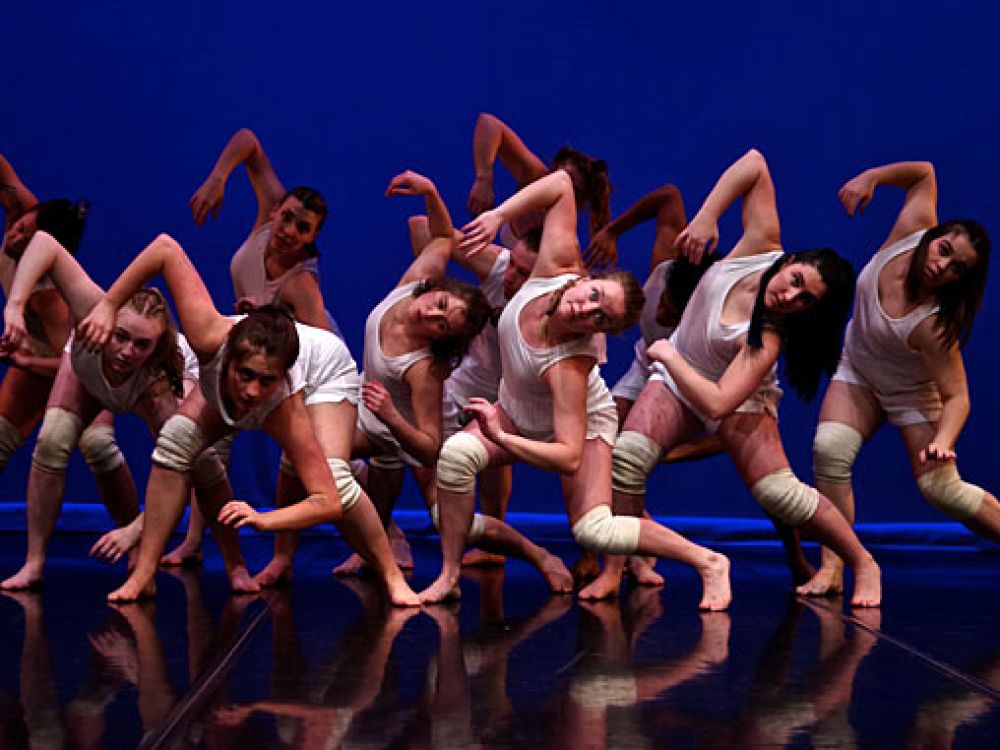 A group of dancers twist on a stage with a blue background