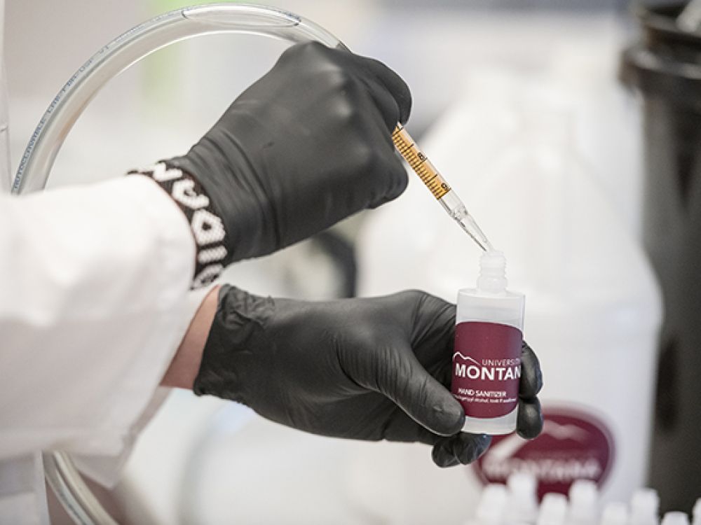 Gloved hands fill a bottle of Griz hand sanitizer.