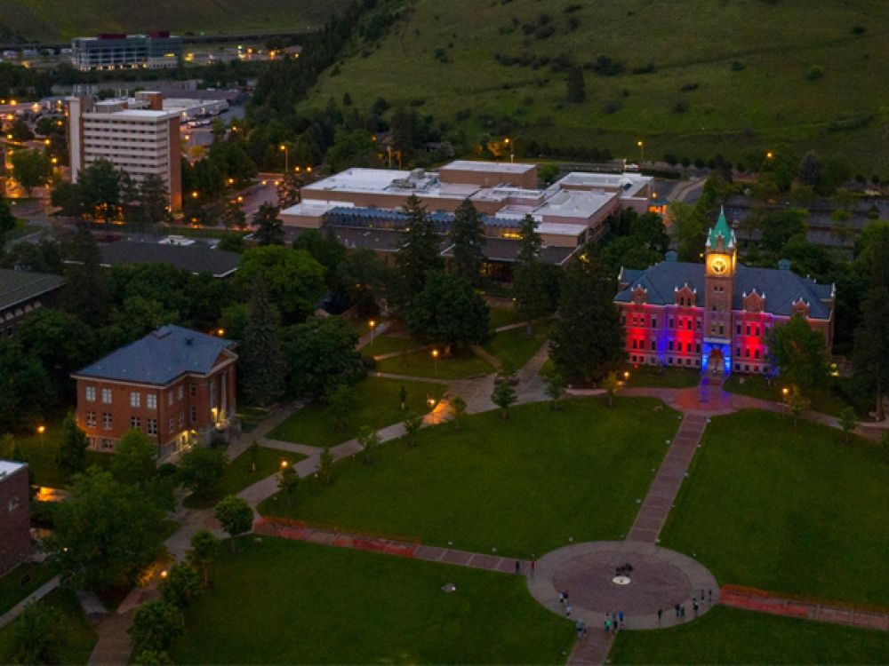 UM's Oval with Main Hall lit in red and yellow as seen from a drone camera