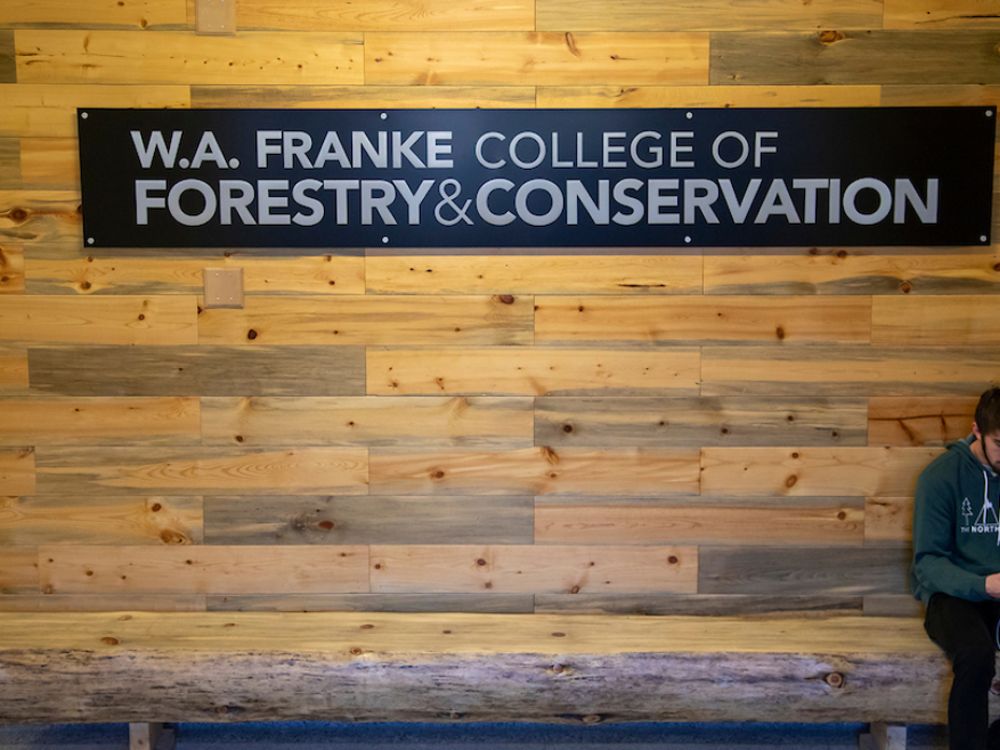 a student sits under a sign that reads W.A. Franke College of Forestry and Conservation