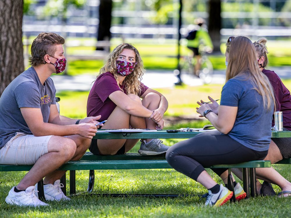 UM students talk at a picnic table on the Oval 