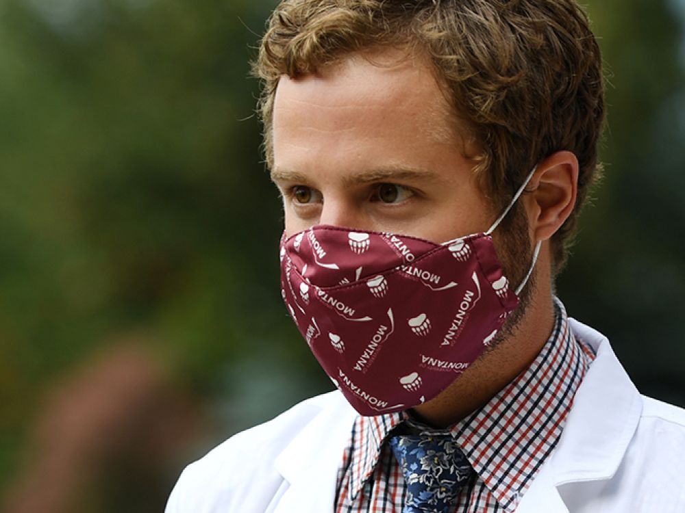 A student with a white medical coat on and a UM facemask
