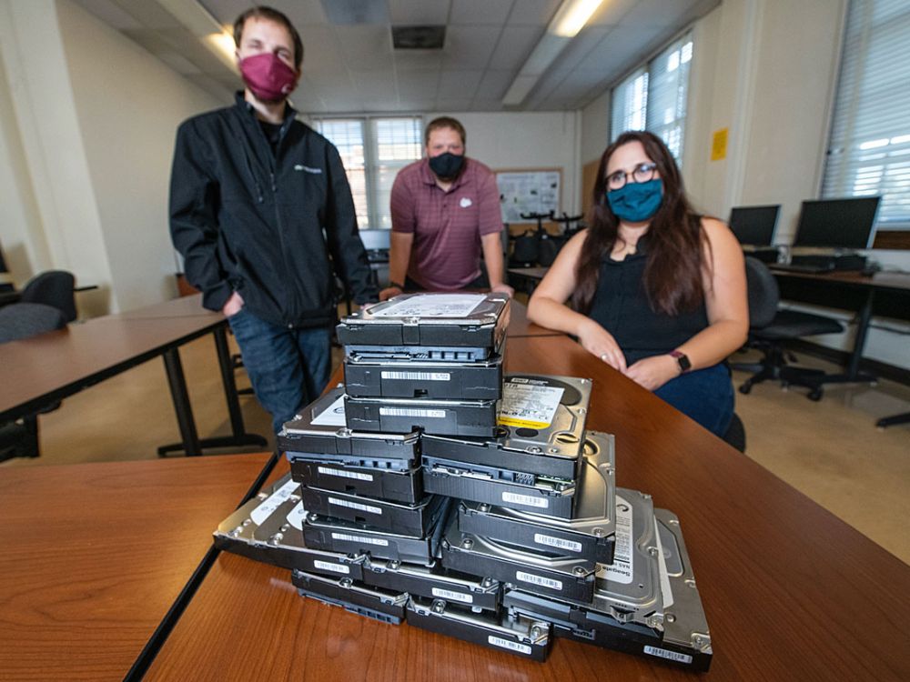 UM doctoral student Tre Bloom (left), acting CIO Zach Rossmiller (center) and Associate Professor Meradeth Snow pose with physical hard disks.