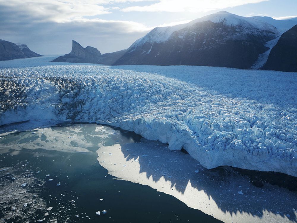 An image of a Greenland ice sheet giving way to water, with mountains in the distance