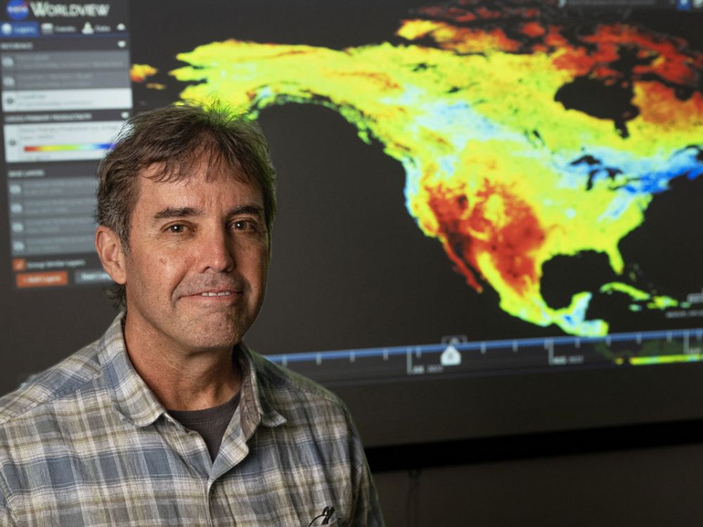 A picture of John Kimball standing before a multicolored video map of the Earth.