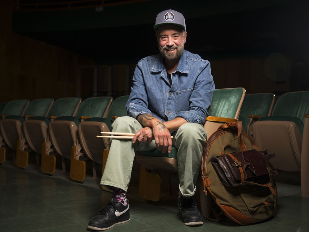 A photo of John Wicks posing with his drum sticks in a classroom at UM. 