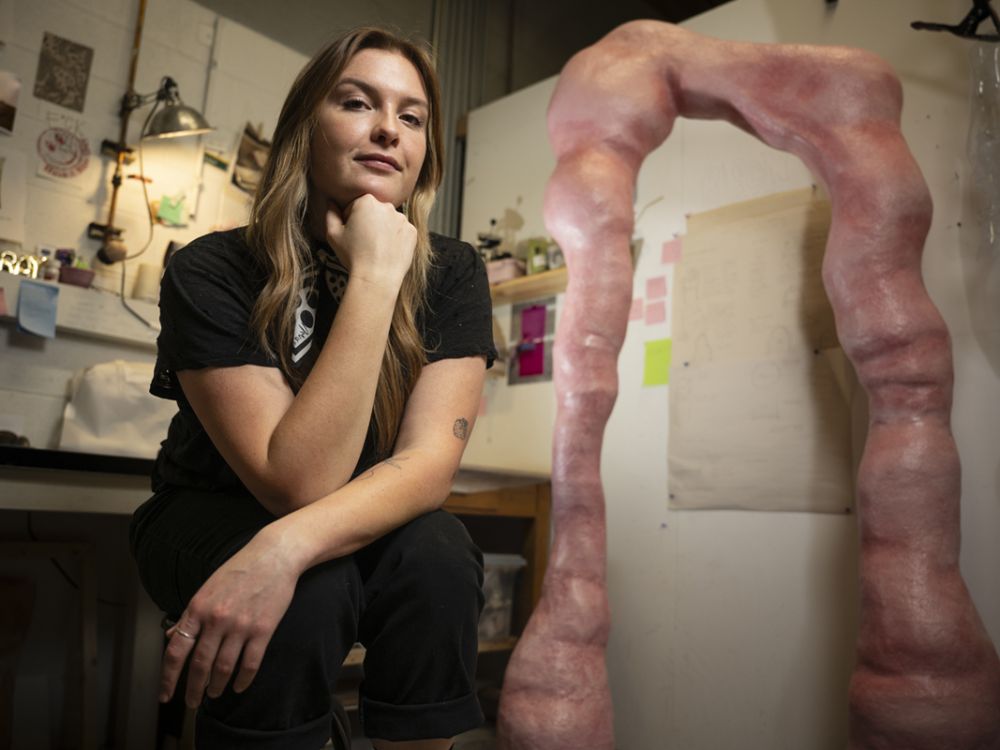 A photo of Emily Mulvaney in her studio next to one of her sculptures. 
