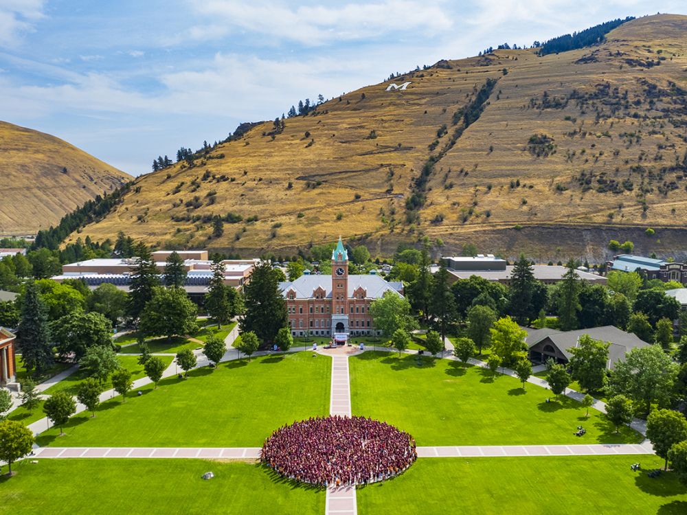 First-year students pose for a photo on the UM Oval with Main Hall in the background.