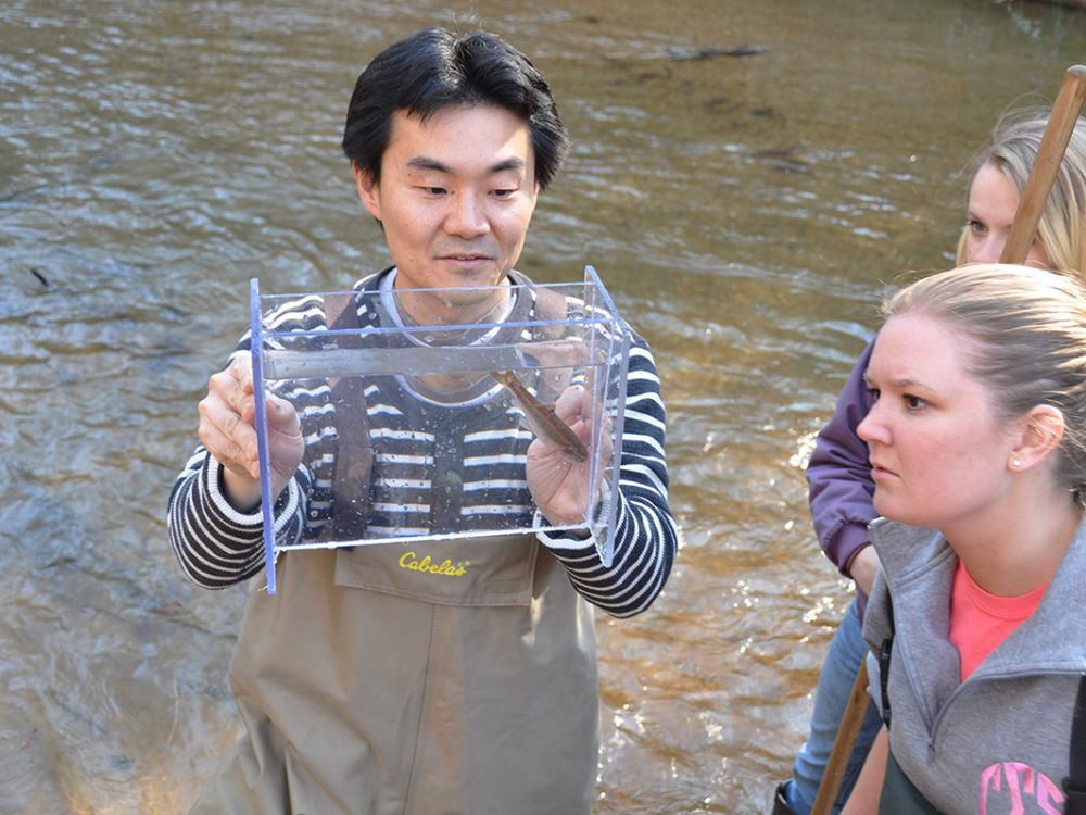 A picture of Yoichiro Kanno holding a fish in a container while standing in water.
