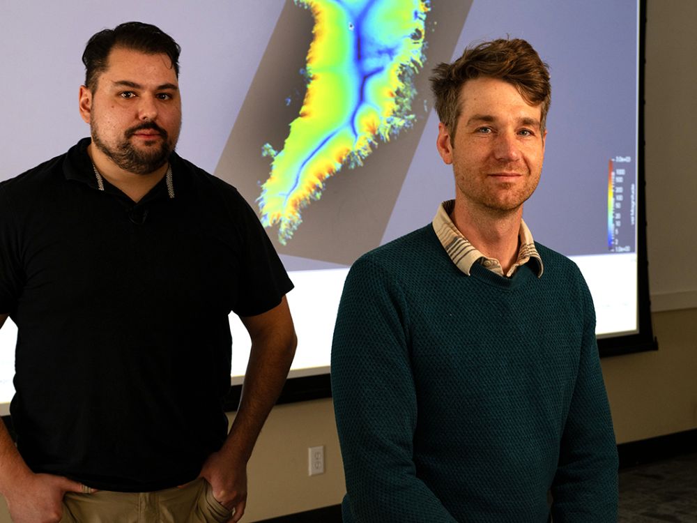 A picture of UM researchers Jacob Downs (left) and Doug Brinkerhoff with a projected map of Greenland between them.
