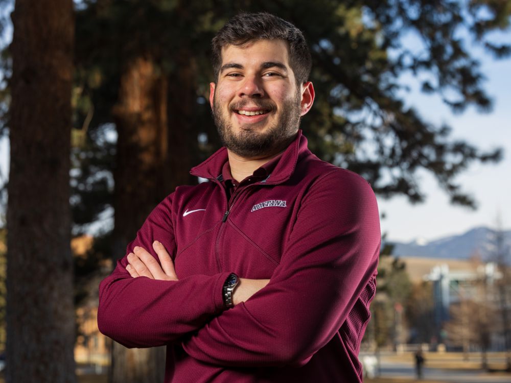 An image of UM student Ryan Fleetwood wearing a UM-branded sweatshirt and standing outside on campus while smiling.