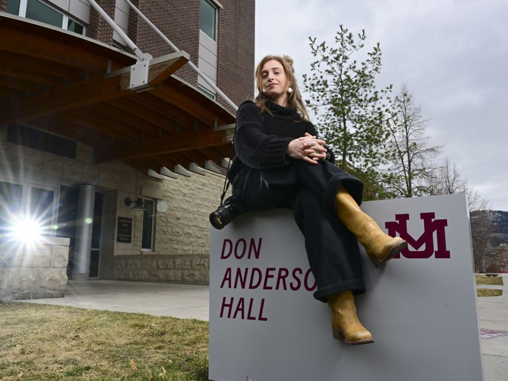 Recent UM journalism graduate Maddie McCuddy sits atop the building sign outside of Don Anderson Hall for a portrait photo.