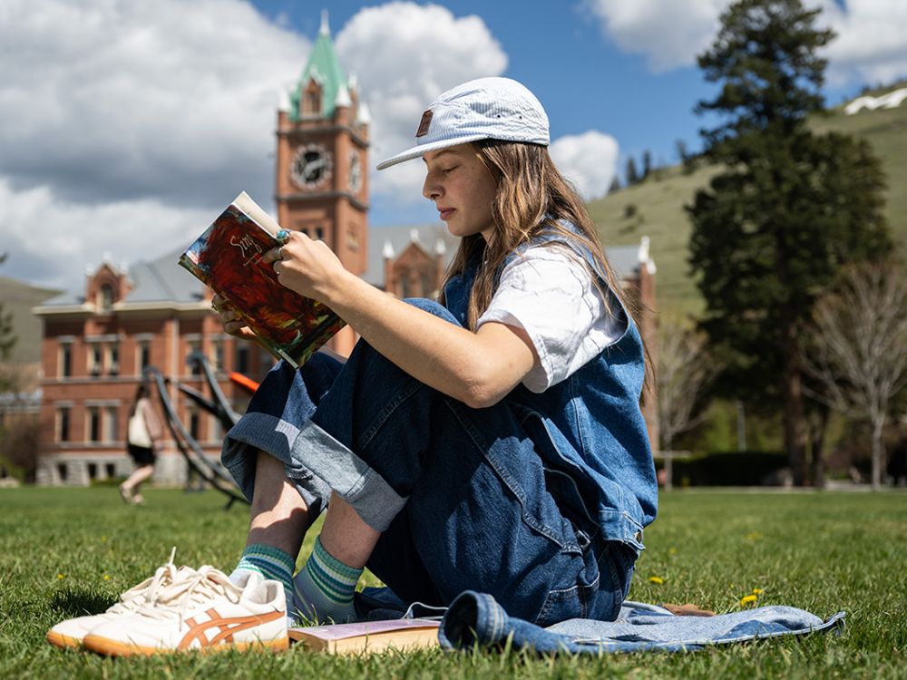 A student reads a book on the Oval before UM's Main Hall.