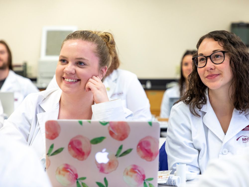 Two UM students sit in a STEM class with white jackets.