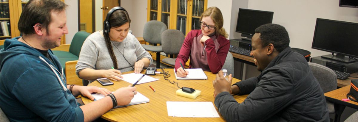 four students sitting around a table listening to each other and taking notes