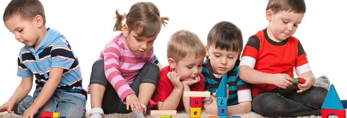 five toddlers sitting in a row playing with blocks