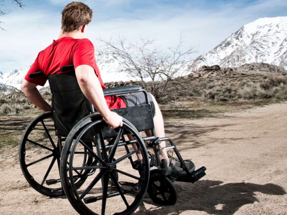 Man in wheelchair going up dirt path with mountain in background