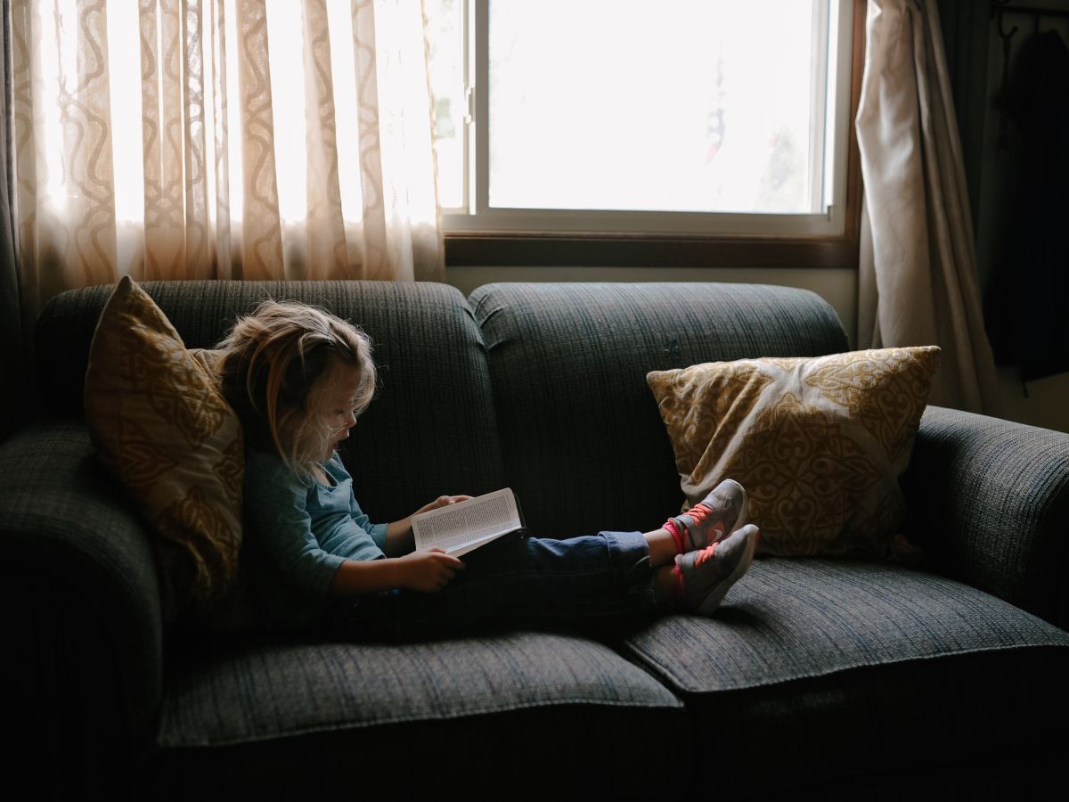 Photo of child on couch reading a book.