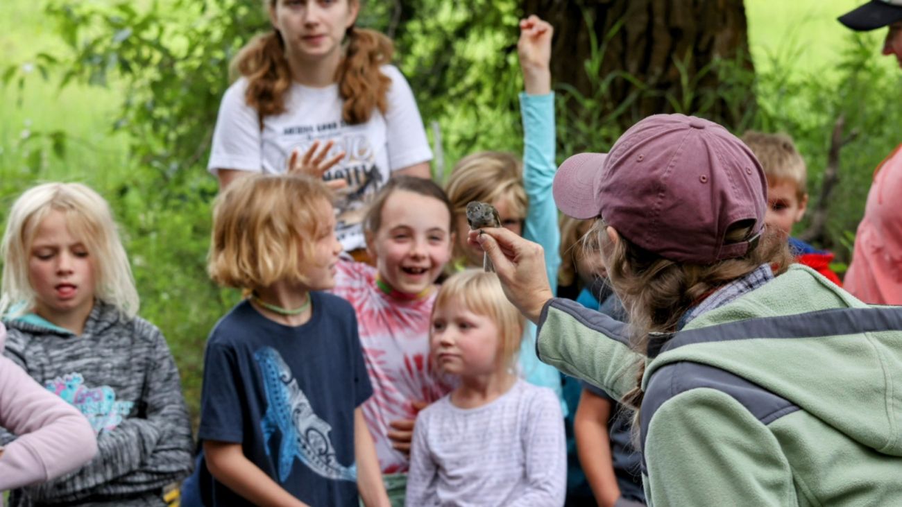 An UMBEL bander showing a bird in the hand to kids gathered around the banding table.