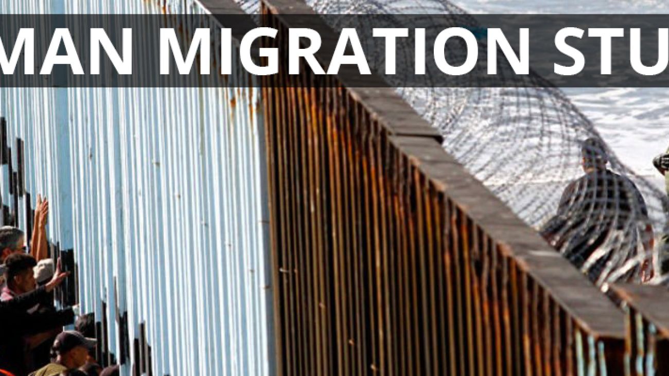 hundreds of people on one side of a fence looking into the other where border protection guards look back