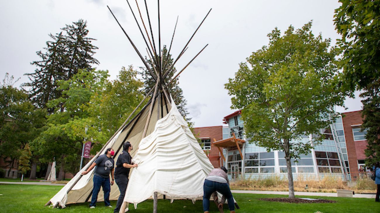 Three students erect a teepee in front of the Native American Center