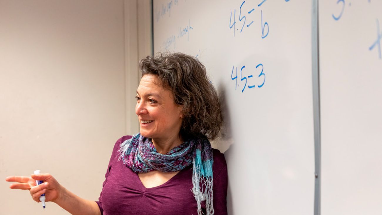 Woman in a pink dress standing in front of a white board with math on it