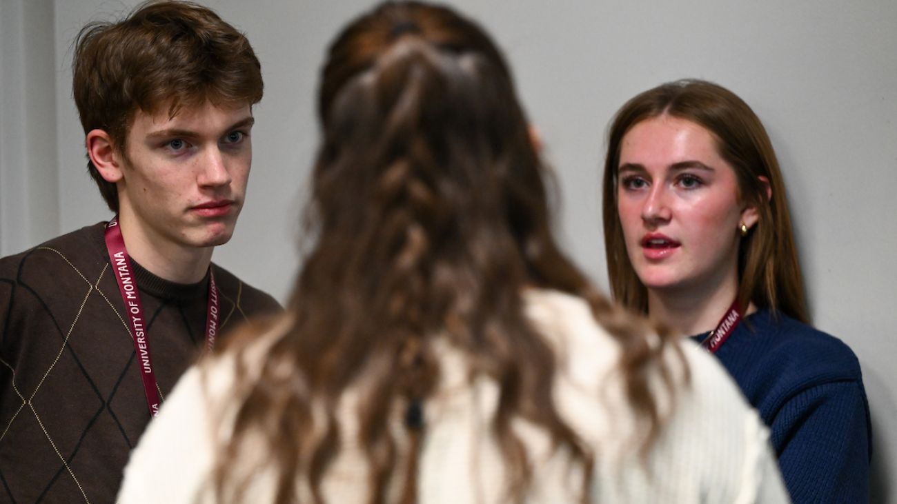 one student seen from behind, two other students staring at her while she speaks