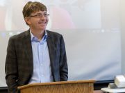 Man with glasses is smiling and giving a speech