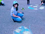 student smiling and kneeling on the pavement with chalk 
