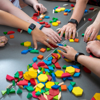 Several hands reaching for colored blocks on a table