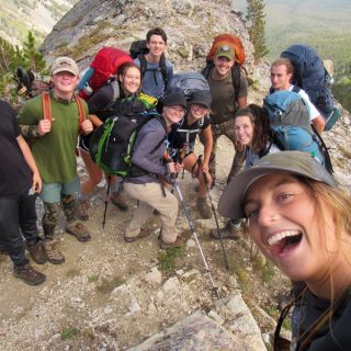 Students stand on a mountain peak and smile for a selfie taken by a member of the Freshman Wilderness Experience.