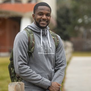UM senior TraJon Cotton leans against a fence and smiles at the camera while wearing a backpack.